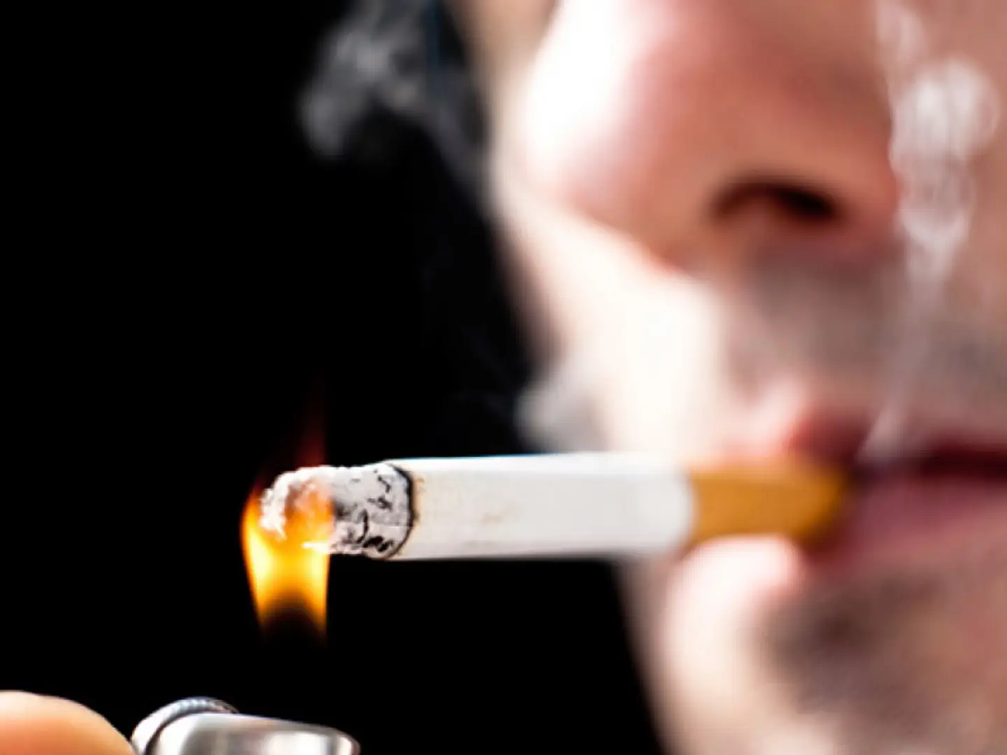 Cigarette being lit by a lighter, close-up view of a person's face in background.