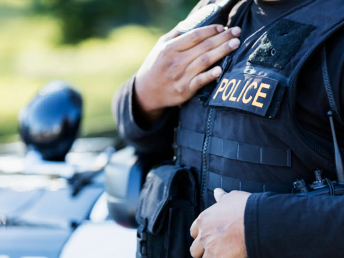 A police officer in uniform with a vest labeled 'POLICE,' standing beside a patrol car.