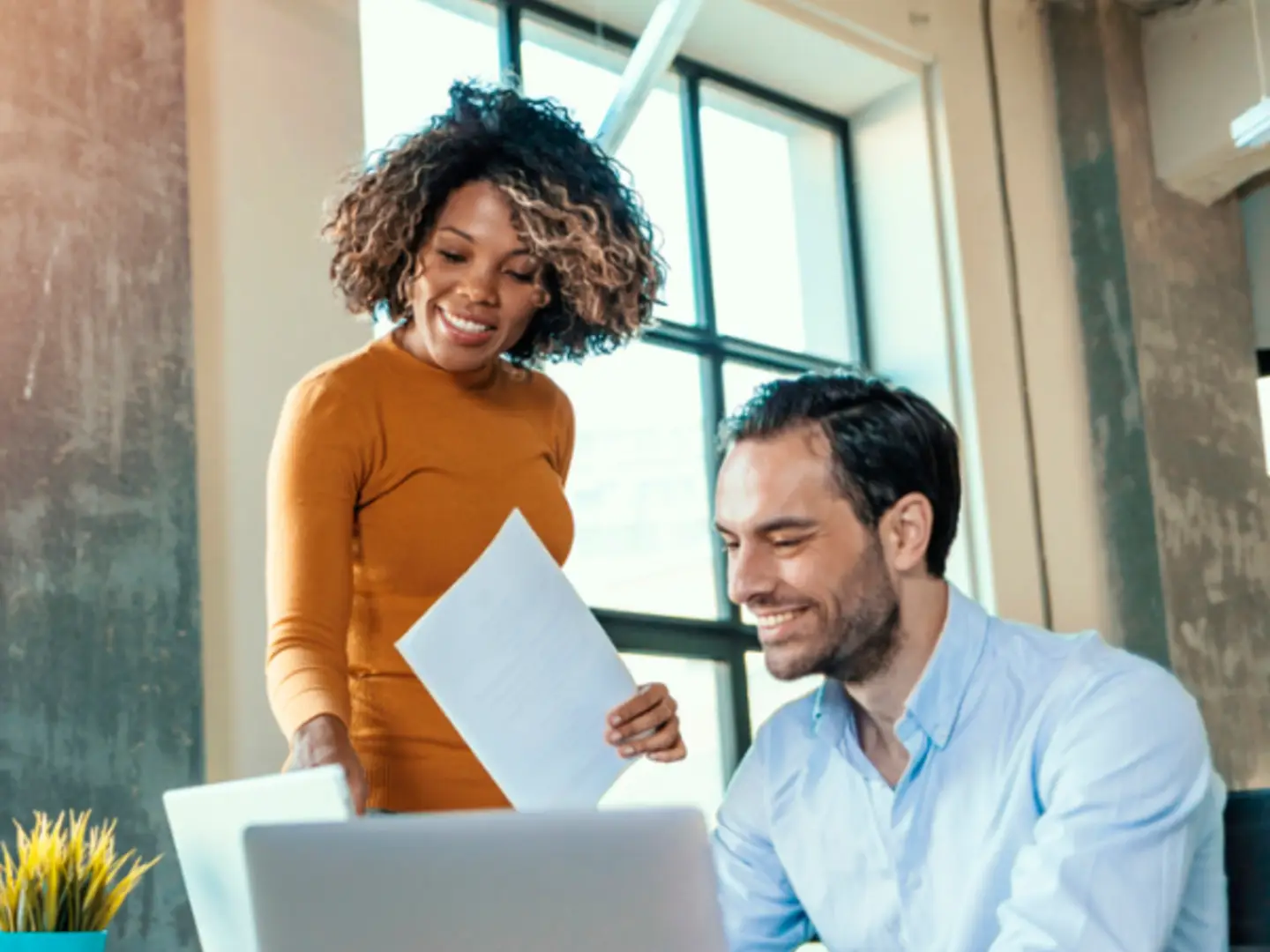 People smiling, discussing documents; modern office with large windows in the background.