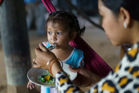 A woman feeds a young child with a spoon in a cozy, indoor setting.