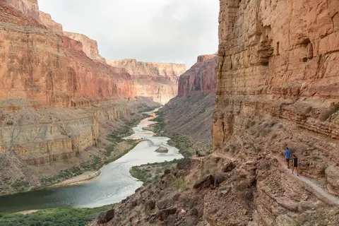 Hikers walking along a cliffside trail overlooking a winding river in a canyon.