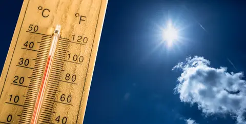 Thermometer showing high temperature under bright sun in a clear sky with scattered clouds.