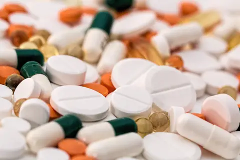 Various pills and capsules scattered, mixed shapes, sizes, colors, on a flat surface.