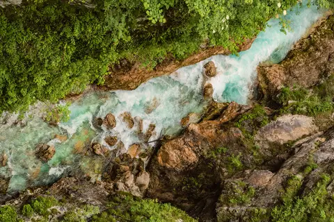 Turquoise river flowing through rugged rocks and lush green forest, viewed from above.