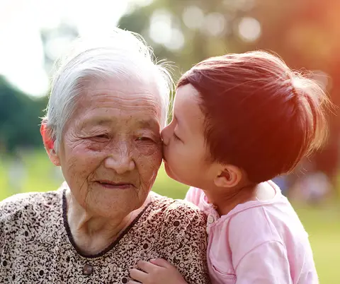 An older Asian woman gets a kiss from her grandchild.