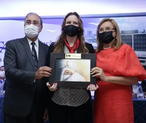 Three masked individuals holding a framed award, with a corporate backdrop and conference setting.