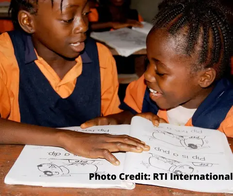 Two girls in school uniforms read a book together in a classroom. Photo Credit: RTI International