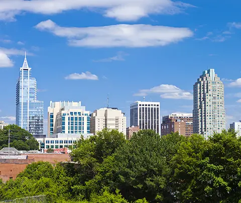 Skyscrapers stand tall against a blue sky, above green trees in an urban cityscape.