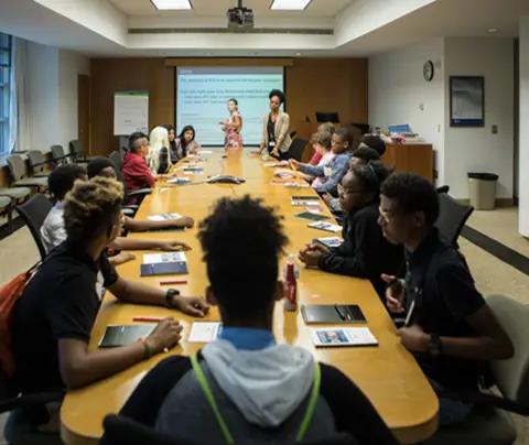 People sit around a conference table listening to two presenters in a meeting room.