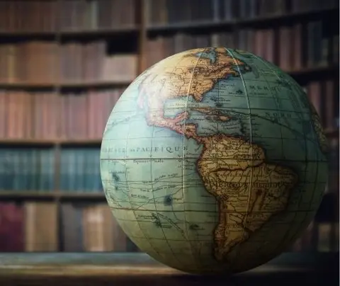 A globe resting on a wooden desk, depicting continents, with bookshelves in the background.