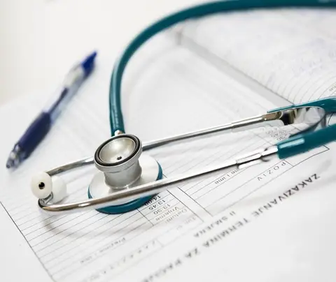 Stethoscope resting on medical documents with a pen nearby in a bright, clinical setting.