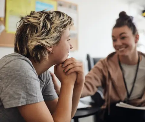 Two individuals engaging in conversation, seated close together in a classroom or office setting.