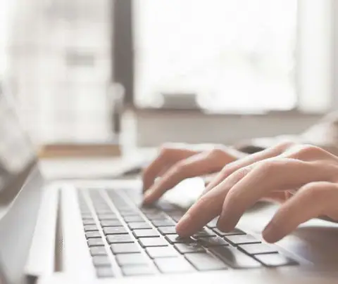 Hands typing on a laptop keyboard in a bright, softly-lit room.