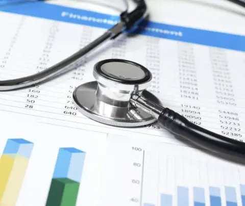 Stethoscope resting on financial documents with charts and graphs in a medical setting.