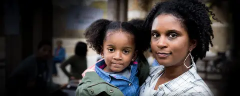 A mother holds a smiling toddler girl.