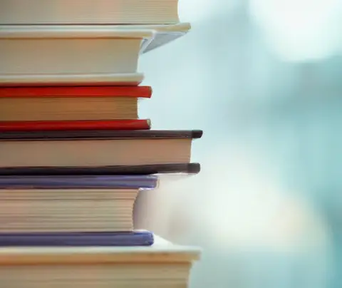 A stack of books rests vertically, showcasing colorful spines against a blurred background.