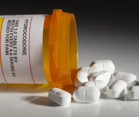 A prescription bottle spills white tablets onto a dark surface, indicating medication for pain relief.