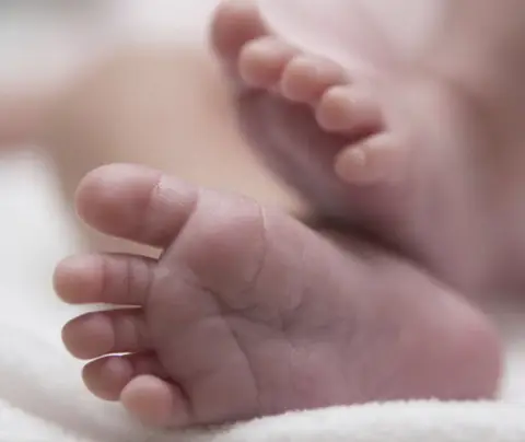 Tiny baby feet curl softly on a white blanket in a tranquil setting.