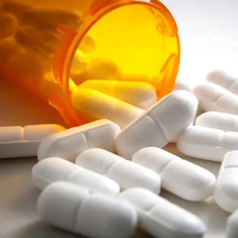 An overturned orange pill bottle spills white capsules onto a light surface.