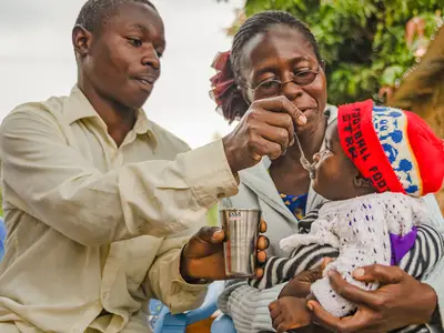 African parents feed a small child with a spoon.