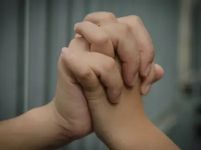 Close up photo of two linked hands, one reaching from behind bars in a correctional facility