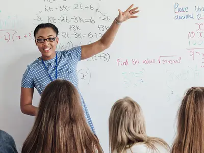 Teacher standing at white board talking to students