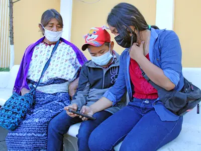 Photo of three people in Guatemala sitting outside together and looking at one of their phones