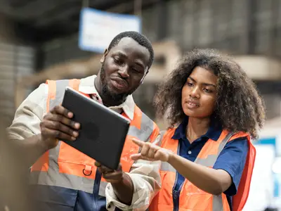 Two workers examine a tablet together in an industrial warehouse.