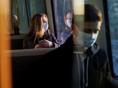 Woman wearing a protective medical mask staring out the window of a bus