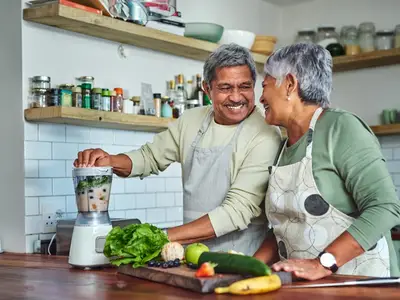 Photo of an elderly couple smiling in their kitchen while cooking a healthy meal