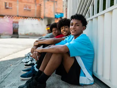 Photo of teenage boys of color smiling while sitting on the street