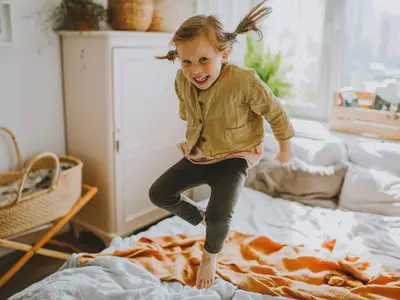 Photo of a girl smiling and jumping on a bed