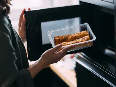 A woman places a plastic tray of food in a microwave.