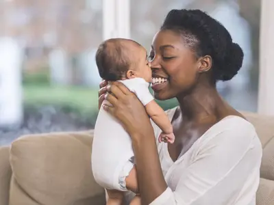 Photo of a young Black mother smiling holding her baby 