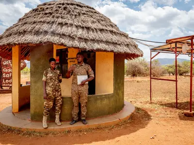 Photo of two uniformed people standing outside a hut in Uganda