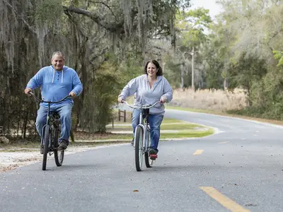 A middle-aged couple riding bikes along a tree-lined road in rural Florida.