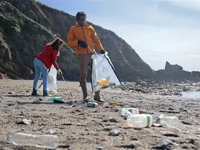 A man and woman picking up plastic bottles on the beach