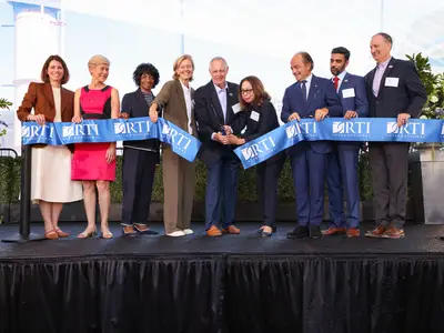 ribbon is cut on stage with large scissors and a group of people is gathered behind the ribbon