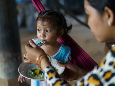 A woman feeds a young child with a spoon in a cozy, indoor setting.