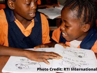 Two girls in school uniforms read a book together in a classroom. Photo Credit: RTI International