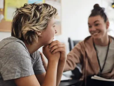 Two individuals engaging in conversation, seated close together in a classroom or office setting.
