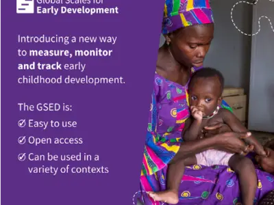 A mother holds a baby while reading about early childhood development tools in a bright room.