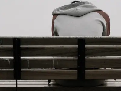 A person suffering from opioid stigma, sitting alone on a bench.