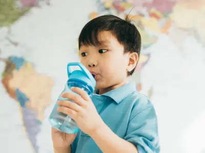 A young Asian child drinking from a water bottle in front of a map