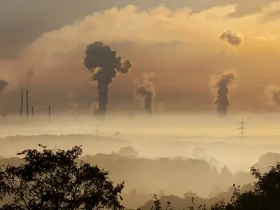 The sun rises over a landscape with factories and smokestacks.