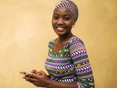 A young African woman reads text messages on a mobile phone.