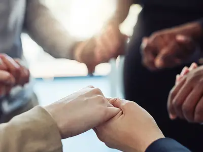 A closeup of a group of people with different skin tones holding hands.