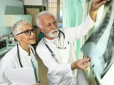 A male and female doctor, wearing lab coats, examine a set of chest x-rays.