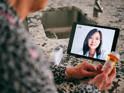 A senior woman meets with her doctor via a teleconferencing app on her phone.