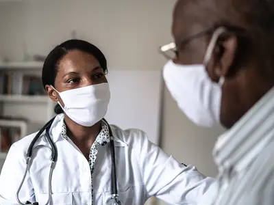 A Black female doctor works with a Black male patient. Both are wearing masks.